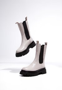 Botines de cuero gris claro con paneles laterales elásticos negros y suelas de goma negras resistentes, con cremallera y lengüeta para facilitar su uso.