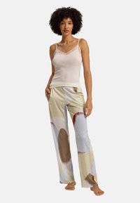 Camisola bianca con pizzo, tessuto morbido; pantaloni larghi e colorati con fantasie a forme astratte in tonalità beige, marrone e blu.