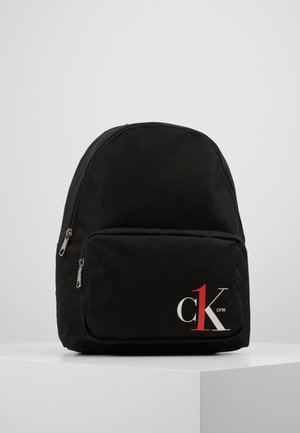 Zwarte rugzak met een voorvak met rits waarin het "ck 1 one"-logo in wit en rood staat, tegen een effen lichtgrijze achtergrond.