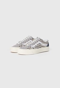 Zapatillas bajas con cordones, de tela tejida en tonos gris, blanco, beige y azul, y suelas de goma en color blanco roto, sobre un fondo liso.