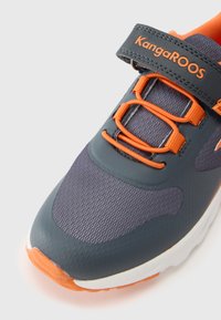 Szürke és narancssárga színösszeállítású sportcipő. Texturált felsőrésszel, sima szintetikus részletekkel és tépőzáras pánttal ellátva.