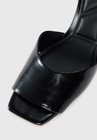 Sandalia de cuero negro con un diseño de punta amplia y abierta, base cuadrada y textura suave. Cuenta con una plantilla acolchada y una estética minimalista.