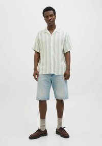 Chemise à manches courtes, boutonnée, avec des rayures verticales vertes et blanches, associée à un short en denim bleu clair et des chaussures marron. Chaussettes gris clair.