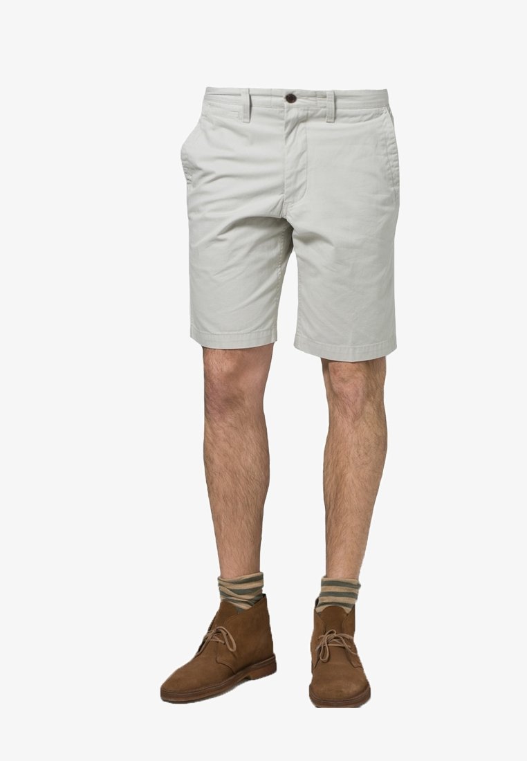 Jasnoszare bawełniane szorty z płaskim przodem, dwoma kieszeniami bocznymi i zapięciem na guzik. Nosi się je z brązowymi zamszowymi botkami do kostki i paskowanymi skarpetkami.