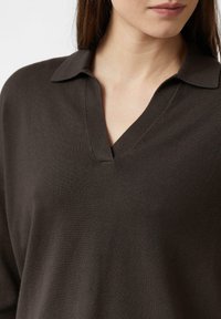 Brązowy pulower z dekoltem w serek i kołnierzem, wykonany z miękkiego, teksturowanego materiału o luźnym kroju. Zbliżenie na linię szyi.