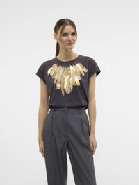 T-shirt gris foncé à manches courtes avec un motif de plumes dorées sur la poitrine ; associé à un pantalon tailleur gris taille haute.
