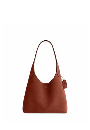 Brązowa skórzana torebka Coach z pojedynczym paskiem na ramię i małą przymocowaną metką z logo na białym tle.