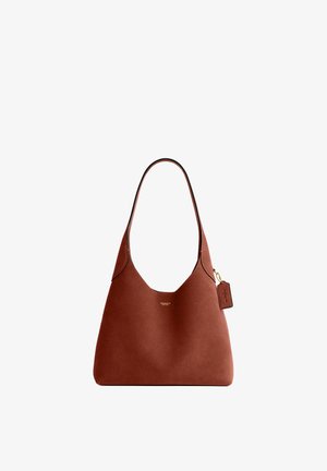 Brązowa skórzana torebka Coach z pojedynczym paskiem na ramię i małą przymocowaną metką z logo na białym tle.