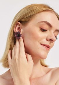 Lille õiekujulised kõrvarõngad, millel on roosa ja must kaunistus ning selged aktsendid, mudeli kõrvas ja pehme nahatooniga.