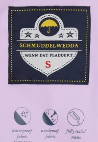 Sötétkék szövet folt sárga és fehér hímzett "SCHMUDDELWEDDA" felirattal, esernyő grafikával és vízállósági útmutatóval.