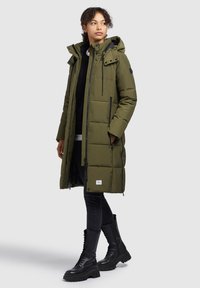 Olive green puffer coat with a hood, zippered pockets, and adjustable drawstrings. Paired with black combat boots and skinny black jeans.