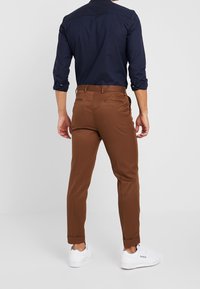Bruna skräddarsydda byxor med slim fit, som har en mjuk textur och uppvikt nederkant, parat med en marinblå långärmad skjorta och vita sneakers.