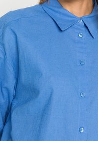 Camicia azzurro chiaro con colletto classico, morbida texture del tessuto e sei bottoni sul davanti.
