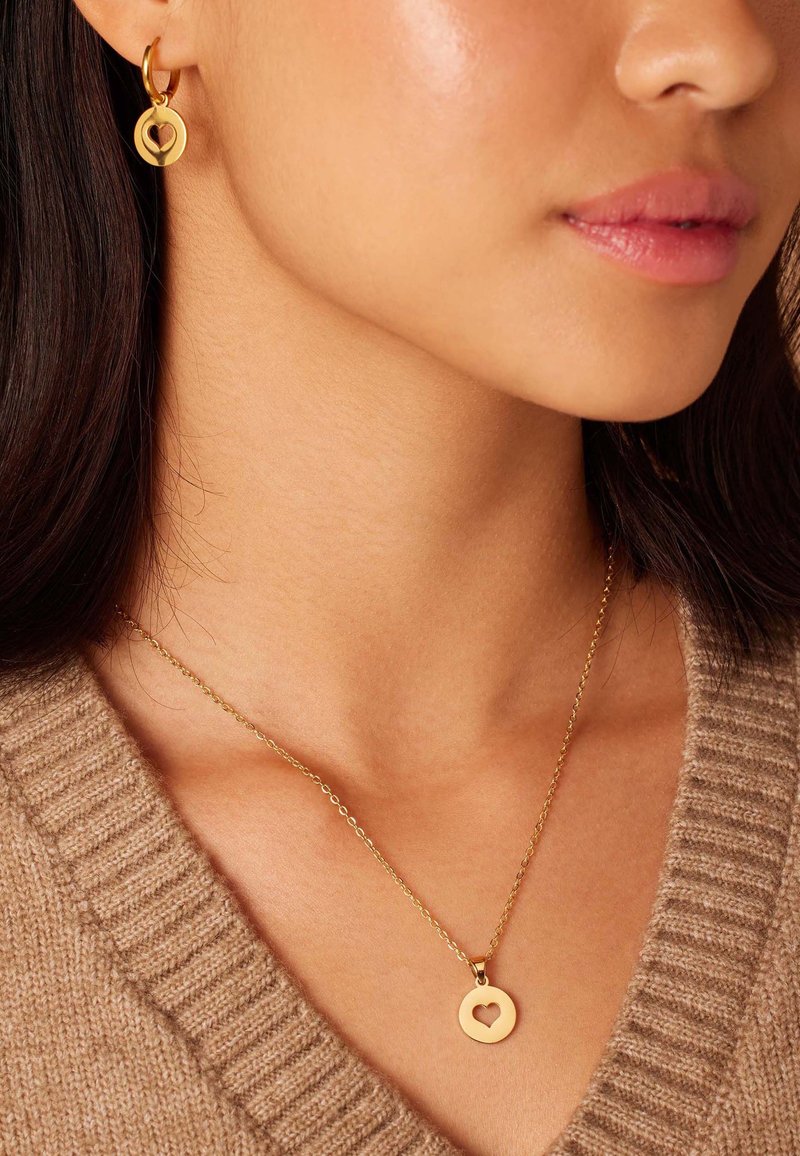 Gouden hoopoorbellen met een cirkelvormige hanger en een hartuitsnede, gecombineerd met een delicate gouden ketting met een soortgelijke hartenhanger.