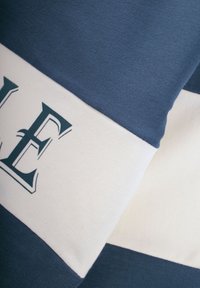 Bawełniana tkanina w kolorze granatowym i białym z poziomymi paskami. Posiada nadrukowany wzór liter w ciemnoniebieskim na białej sekcji, gładka struktura.