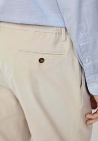 Pantalones de pantalón de pana color beige claro con un bolsillo trasero con un botón marrón. Combinados con una camisa azul de botones con un patrón texturizado.