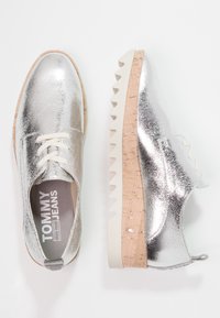 Souliers argent métallisés à lacets avec une surface texturée, dotés d'une plateforme en liège beige et d'une semelle extérieure crantée blanche. Logo visible à l'intérieur.