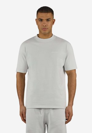 Mann trägt ein passendes hellgraues kurzärmeliges T-Shirt und Shorts, steht vor einem schlichten weißen Hintergrund.
