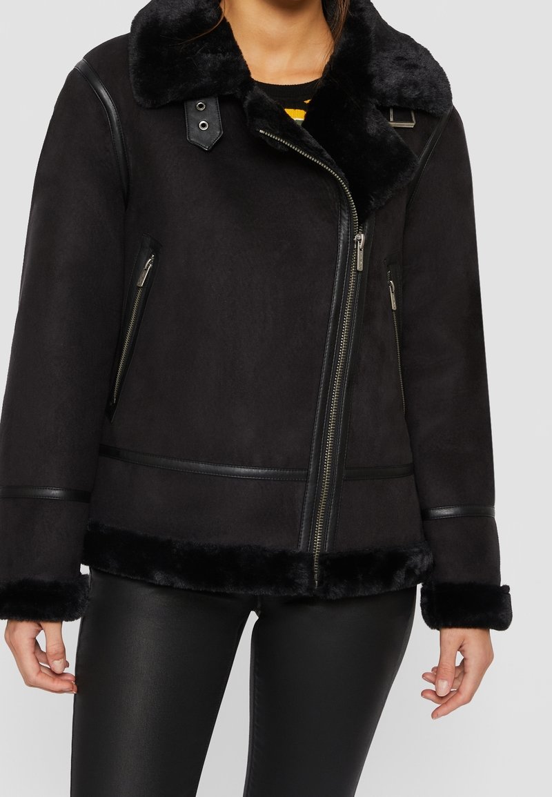 Veste noire doublée de fausse fourrure avec un col, des accents en cuir, des fermetures éclair et une finition lisse, présentant une coupe décontractée et un ourlet raccourci.