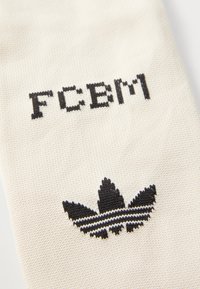 Beez sokk musta kudumitekstiga "FCBM" ning heraldi märgiga, millel on kolm lehte ja kaks musta triipu all.