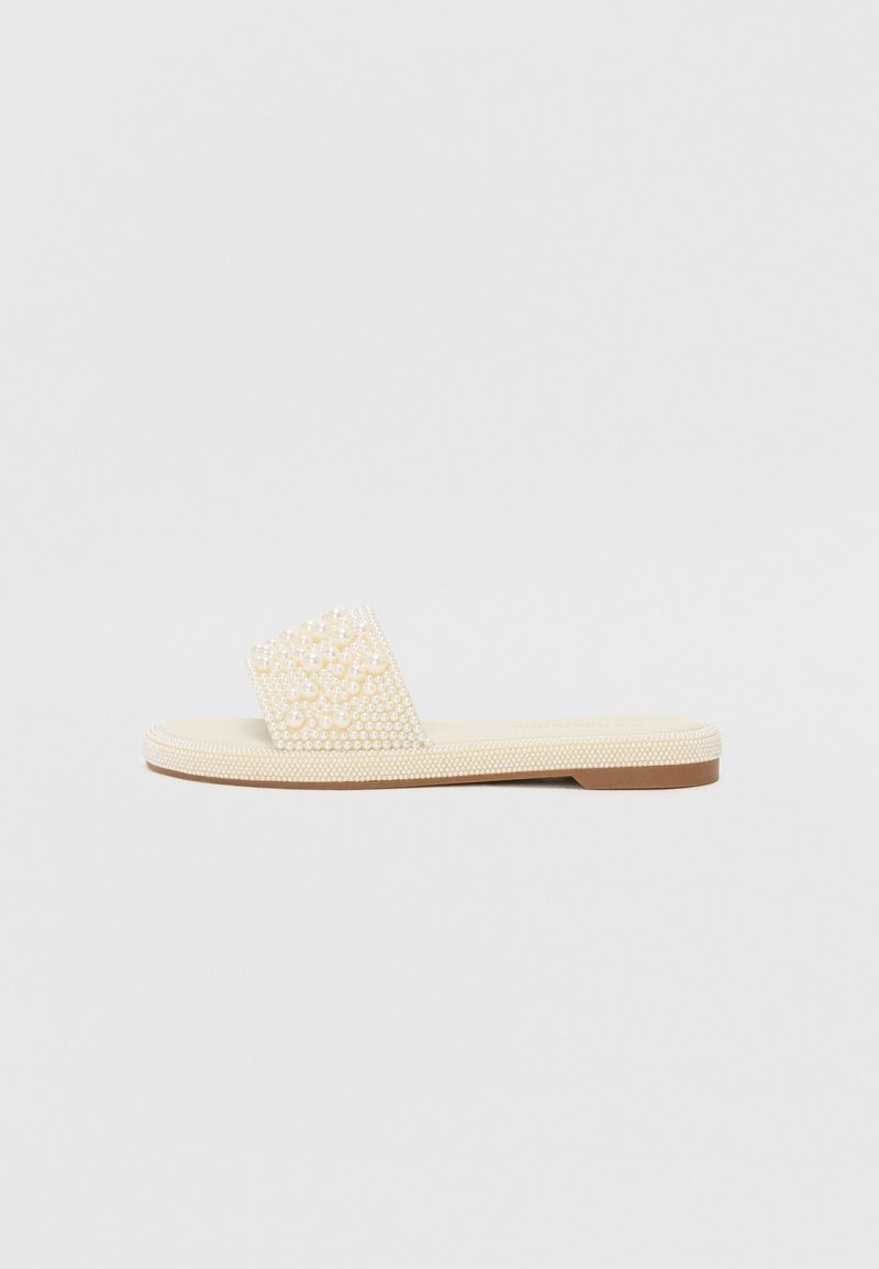 Sandale à glissière beige avec une semelle texturée, présentant un dessus décoratif orné de petites perles semblables à des perles. Design plat, profil minimal.