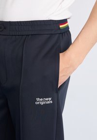 Calças de jogging azul-escuro feitas de um material suave, com um logótipo bordado em branco, uma cintura com riscas multicoloridas e bolsos laterais.
