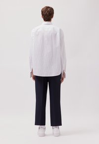 Camicia oversize a righe bianche e blu con orlo curvo, abbinata a pantaloni larghi blu navy e sneakers bianche.