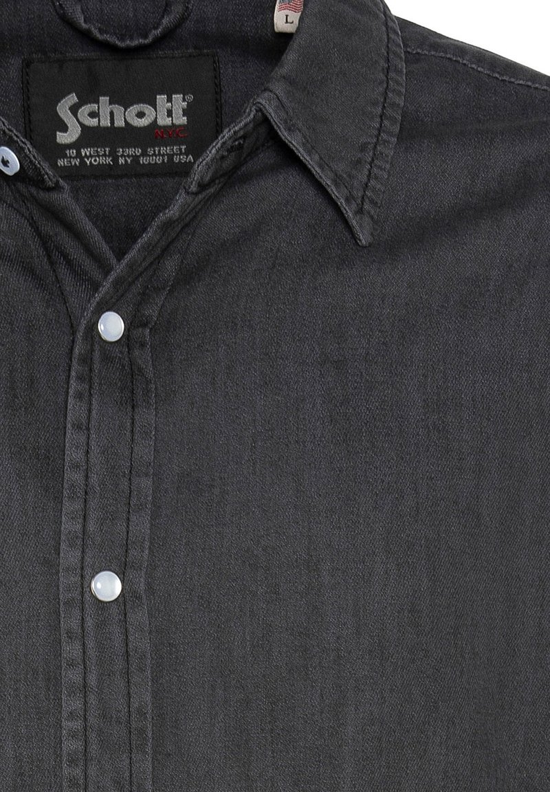 Chemise gris foncé à boutons pression nacrés, col pointu et étiquette noire portant "Schott NYC" avec l'adresse en texte blanc.