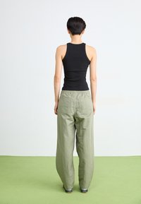 Zwarte geribde tanktop gecombineerd met wijde, lichtgroene broek. De outfit heeft een eenvoudig ontwerp en een ontspannen silhouet.