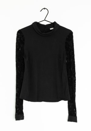Black long-sleeve top with a high neckline. Solid fabric on body and sheer lace on sleeves. Cuffs in solid black fabric, hanging on a hook.
