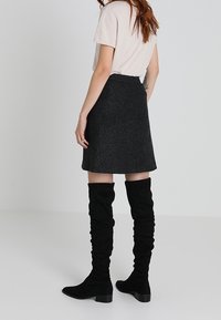 Jupe noire en mélange de laine avec une texture subtile, associée à des bottes en suède noires jusqu'aux genoux présentant un design décontracté et un bout carré.