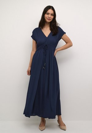 Abito lungo blu navy con scollatura a V, maniche corte, vita con cordoncino e tessuto fluido. Abbinato a ballerine beige a punta.