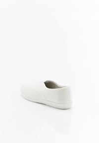 Zapatilla slip-on blanca de lona con punta redonda, paneles laterales elásticos y un interior a rayas. Suela plana con un acabado suave.