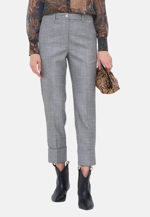 Pantalon court à carreaux gris avec des poignets, porté avec des bottines noires et un haut à motifs, tenant une pochette marron en cuir de serpent.