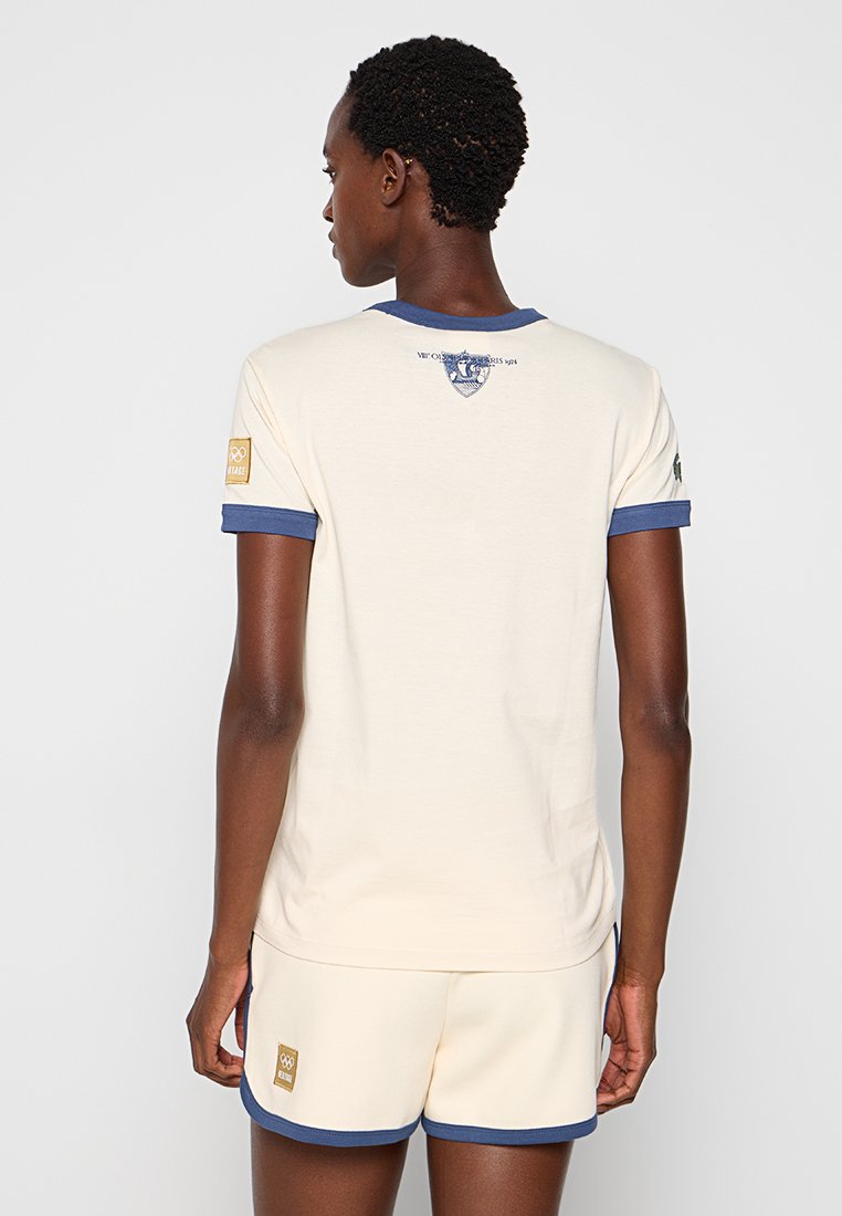 Cremfarbendes T-Shirt mit marineblauen Besätzen am Kragen und an den Ärmeln, versehen mit einem gedruckten Emblem auf der Rückseite, kombiniert mit passenden Shorts.