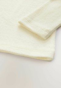 Kremowa tkanina polarowa o miękkiej, teksturowanej powierzchni. Posiada złożony rękaw oraz wykończenie szwów na hemie.