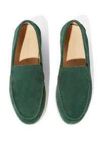 Ciemnozielone zamszowe buty wsuwane z zaokrąglonym noskiem, widocznym przeszyciem i kremową podeszwą. Prosty, elegancki design.