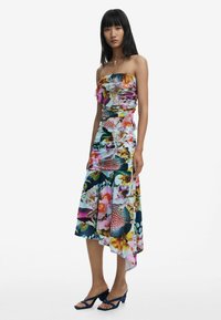 Floral strapless dress with vibrant colors, gathered fabric, asymmetrical hem, and a soft texture. Worn with navy strappy heels.