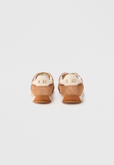 Scarpe sportive in suede marrone con collo bianco e dettagli del logo dorato. Presentano una suola in gomma e una lavorazione a contrasto.