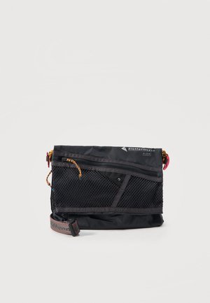 Μαύρη τσάντα crossbody με μπροστινή τσέπη από δίχτυ, κλείσιμο με φερμουάρ, ρυθμιζόμενο υφασμάτινο λουράκι και μικρή μπαζίτσα με λογότυπο στην πάνω δεξιά γωνία.