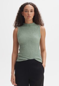 Lichtgroene mouwloze top met een textuur, kreukelige ontwerp en een geraffineerde hoge halslijn. Gecombineerd met zwarte aansluitende broek.