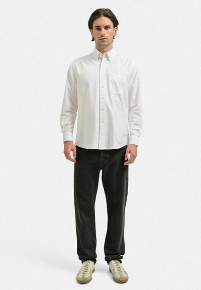 Vit långärmad skjorta med knappar och ficka, i kombination med svarta jeans och beige sneakers. Tyget verkar vara slätt med en vanlig passform.