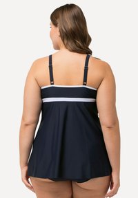 Námořnický plavecký tankini s nastavitelnými ramínky, bílými akcentovými pruhy, rozevlátým spodním lemem a měkkou, elastickou tkaninou navrženou pro pohodlí.