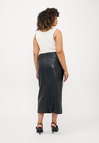 Μαύρη δερμάτινη φούστα midi με εφαρμοστή σιλουέτα, δύο πίσω τσέπες και ορατές ραφές. Συνδυασμένη με ένα λευκό τοπ με τιράντες και ψηλοτάκουνα.