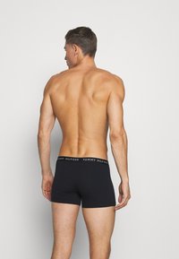 Schwarze Boxershorts mit einem markierten Bund, die ein eng anliegendes Design und eine glatte Stofftextur aufweisen, von hinten betrachtet.