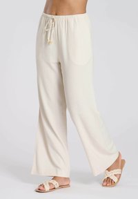 Pantalons larges beige clair en tissu doux. Dotés d'une taille élastique avec cordon de serrage et de deux poches latérales.