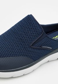 Navy mesh slip-on shoe with a textured upper, contrasting navy rubber sole, and Skechers logo on the side. Curved design and flexible fit.