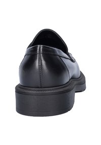 Zwarte leren instapper met dikke zwarte rubberen zool, zichtbare stiksels op de hak, bekeken vanuit de achterkant op een witte achtergrond.