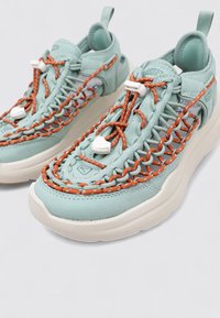 Zapatillas de running azul claro con detalles en cordones naranjas, suela blanca gruesa y upper texturizado. Cuentan con una cinta en el talón para facilitar su uso.