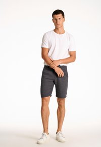 Shorts rayés gris en tissu léger, associés à un t-shirt blanc uni et des baskets blanches, offrant une coupe décontractée et un design simple.